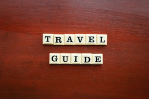 the word travel guide spelled with scrabble tiles