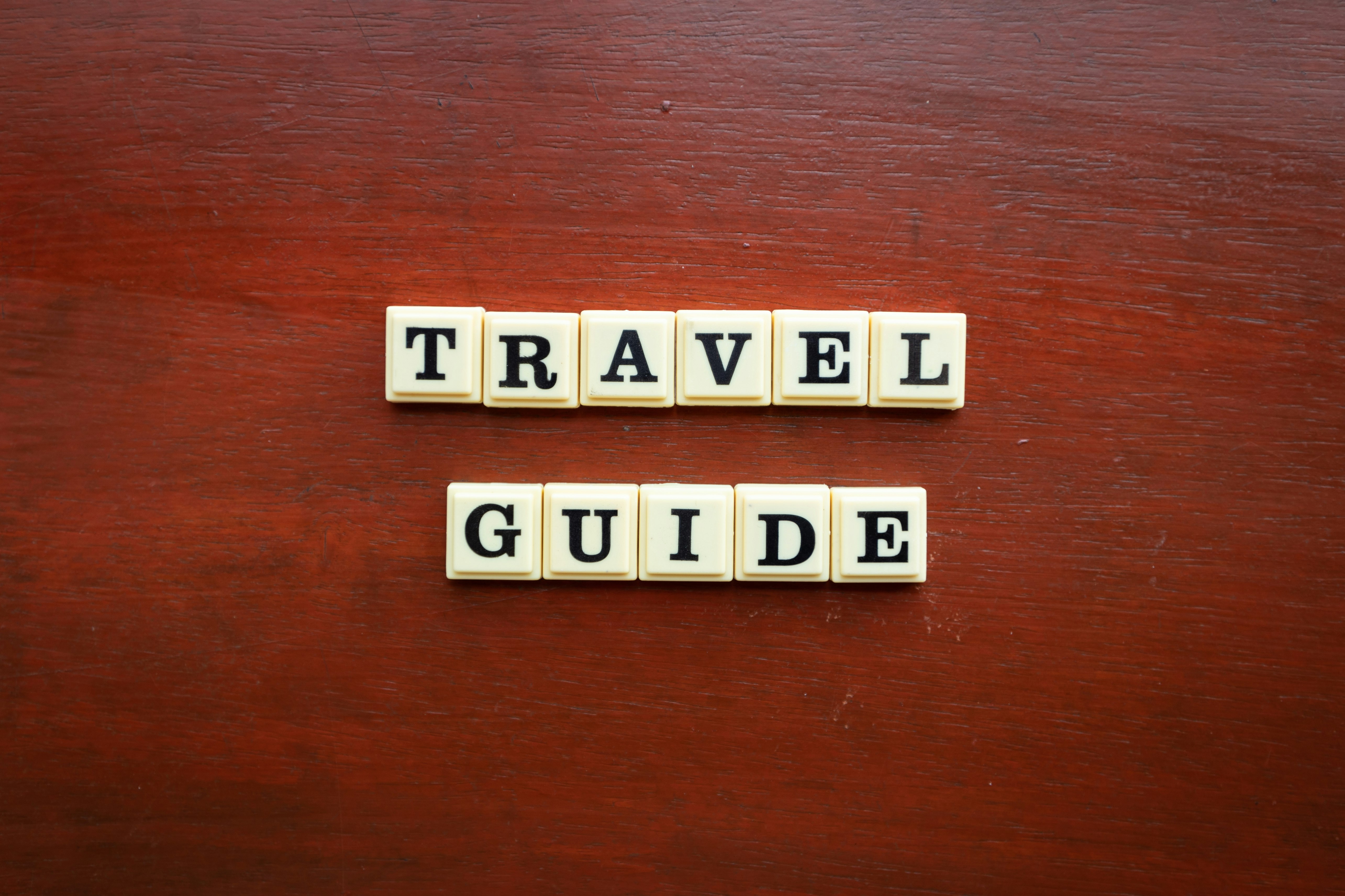 the word travel guide spelled with scrabble tiles