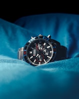 Sporty chronograph watch with a sleek black leather strap resting on polished black glass.