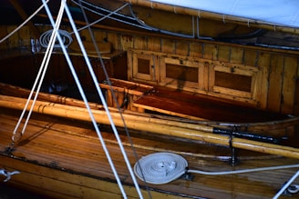 An interior of a wooden boat featuring polished wooden surfaces and multiple ropes coiled neatly. The cabin walls have a warm, honey-colored finish with a few rectangular panels. Slight reflections hint at a glossy sheen on the wood.