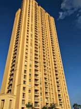Elegant high-rise residential building with maroon and beige accents under a clear sky.