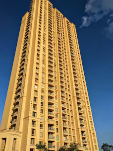 Elegant high-rise residential building with maroon and beige accents under a clear sky.