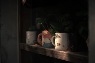 A close-up of vibrant hand-thrown ceramic mugs stacked on a wooden shelf bathed in warm sunlight.