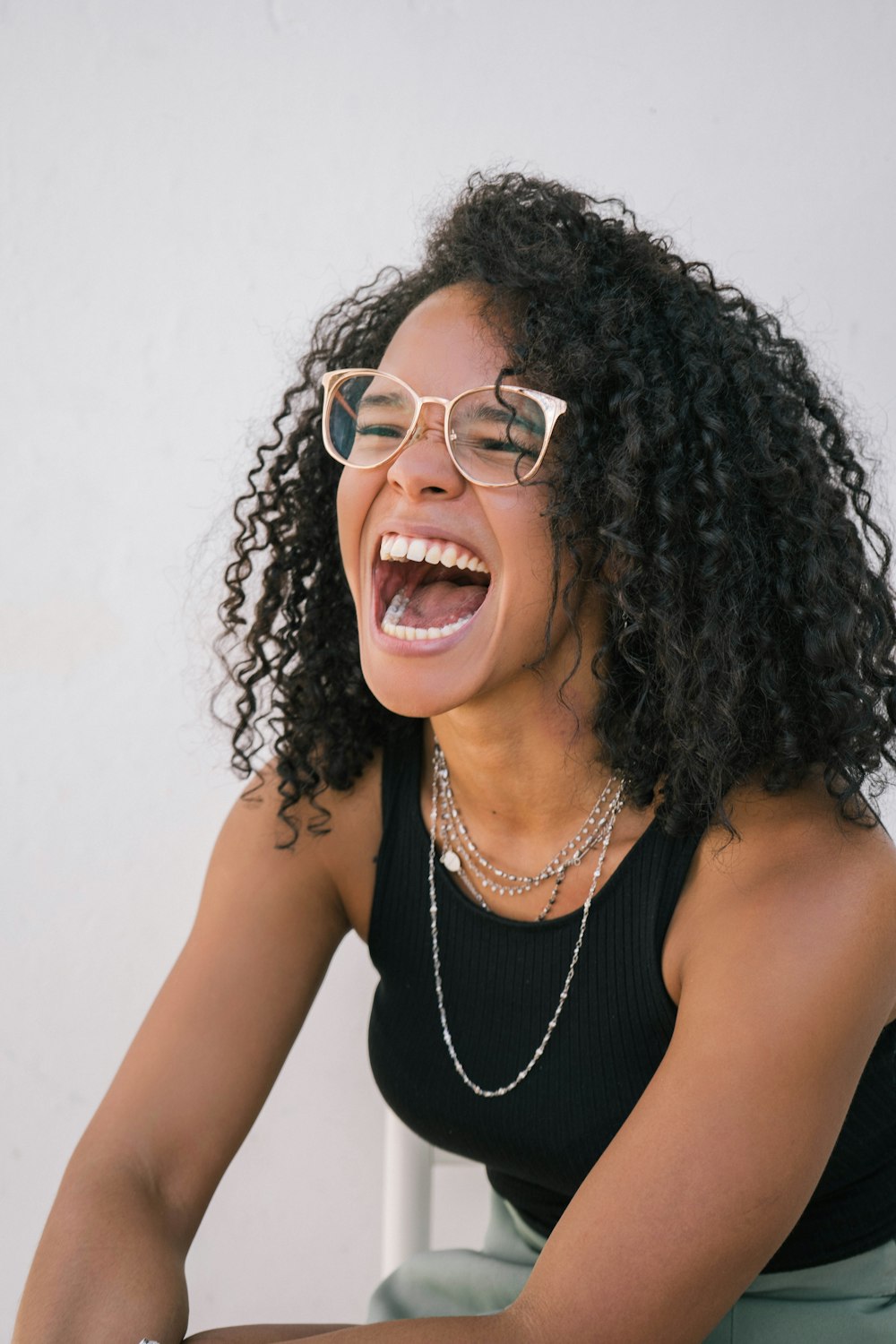 a woman wearing glasses and laughing while sitting on a chair