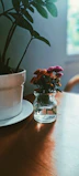 Colorful pottery pieces around a small handmade vase filled with fresh flowers in natural light.
