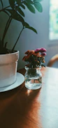Colorful pottery pieces around a small handmade vase filled with fresh flowers in natural light.