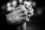 Close-up of hands holding a white cane, symbolizing trust and care in a warm red and black setting.