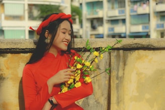 A young woman wearing a bright floral dress posing cheerfully on a colorful urban street.