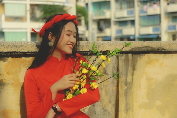 A young woman wearing a bright floral dress posing cheerfully on a colorful urban street.