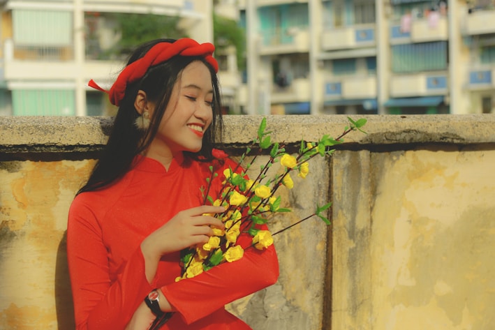 A cheerful young woman wearing a bright floral dress, smiling in a sunlit urban setting.