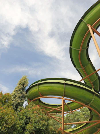 A tall, wet waterslide with children sliding down laughing, surrounded by green grass and trees.