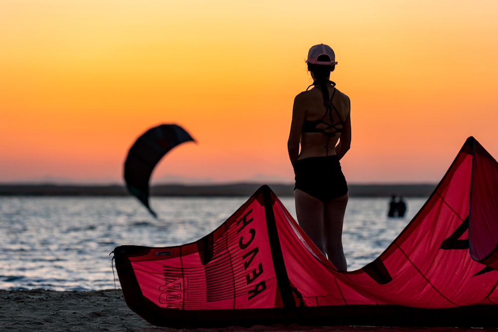 a woman standing on a beach next to a red kite