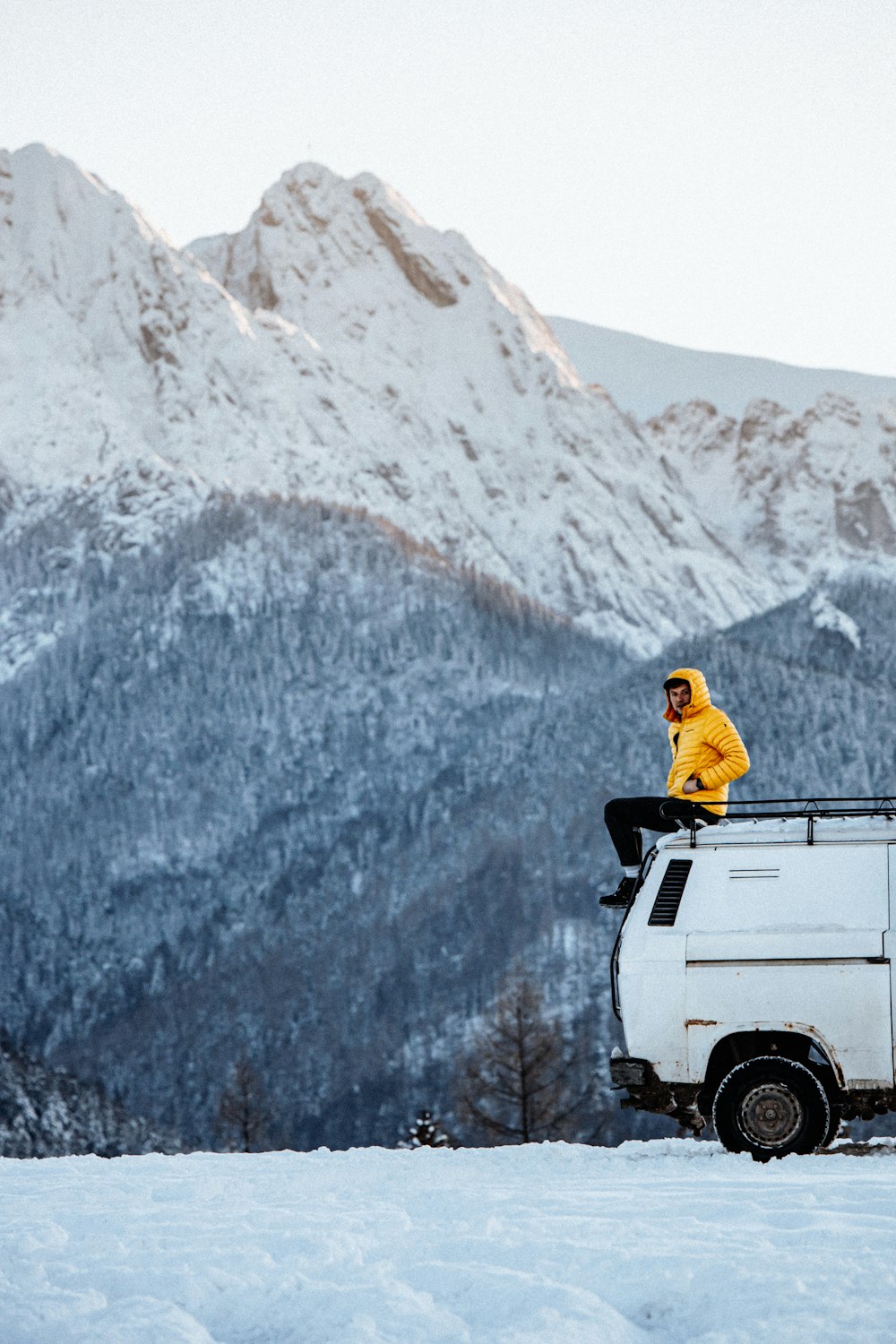 a man sitting on top of a van in the snow