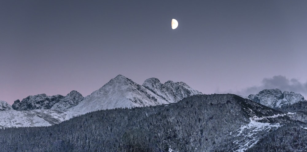 a full moon is seen over a snowy mountain range