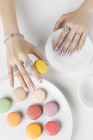 Hands decorating delicate macarons with pastel-colored icing in a bright kitchen.