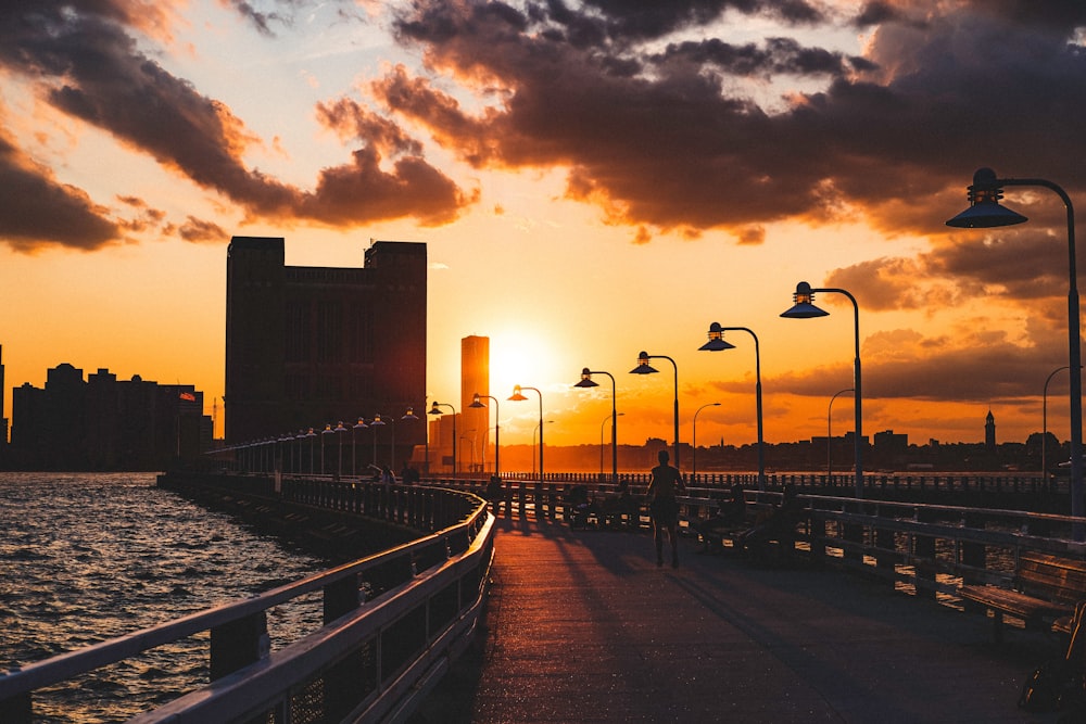 the sun is setting over the water near a pier