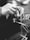 A close-up black and white photo of hands weaving threads, suggesting skilled craftsmanship or an artisanal process. The hands are manipulating thin, delicate strands, indicative of intricate handiwork.