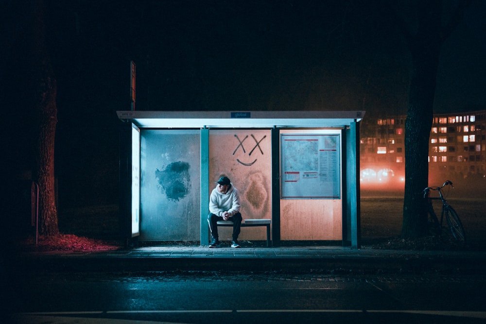 a man sitting on a bench in front of a bus stop