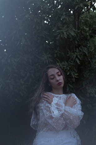 A serene woman outdoors with eyes closed, taking a slow, mindful breath surrounded by greenery.