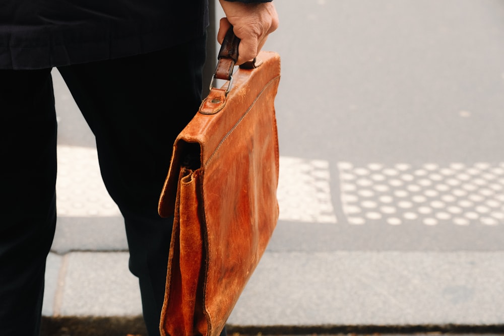 a person holding a brown briefcase on a sidewalk