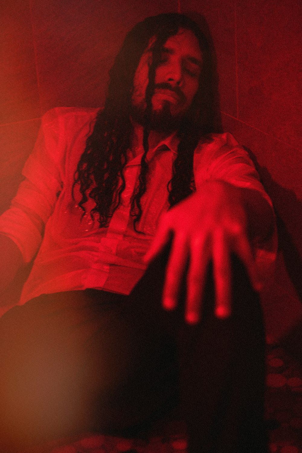 a man with long hair sitting in a dark room