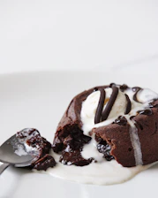 Close-up of a chocolate lava cake with molten center oozing out, garnished with a dusting of powdered sugar and a sprig of mint.