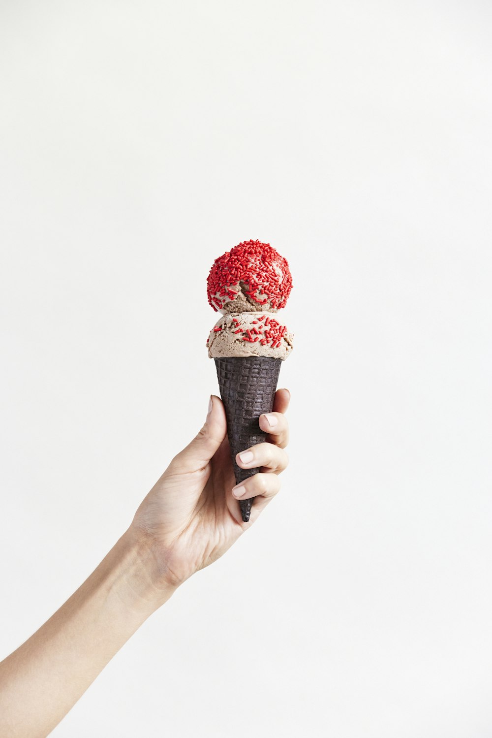 a hand holding an ice cream cone with sprinkles