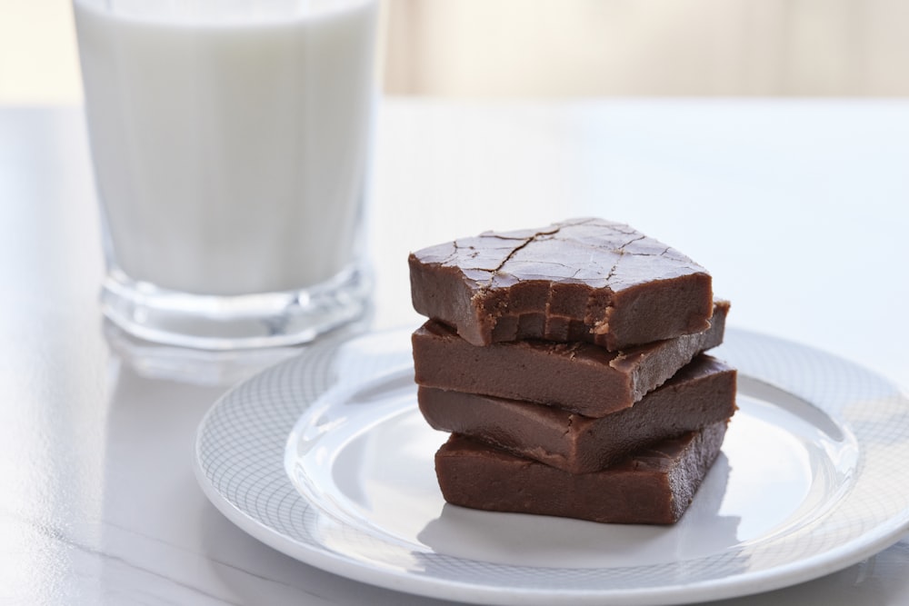 three pieces of chocolate on a plate next to a glass of milk