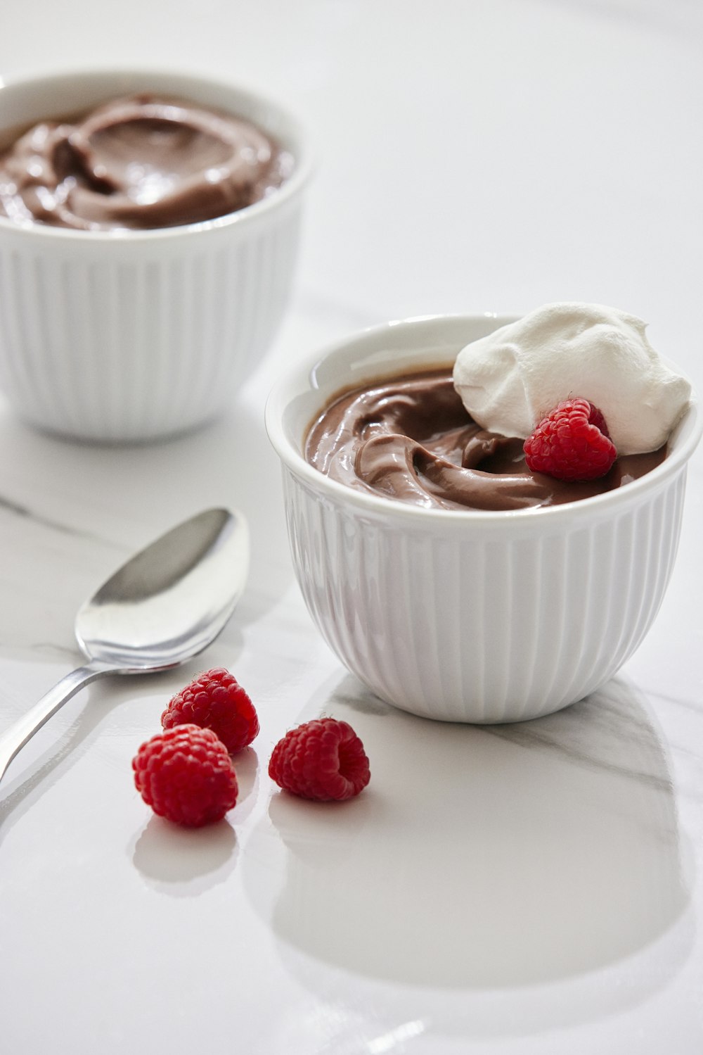 two bowls of chocolate pudding with raspberries on the side