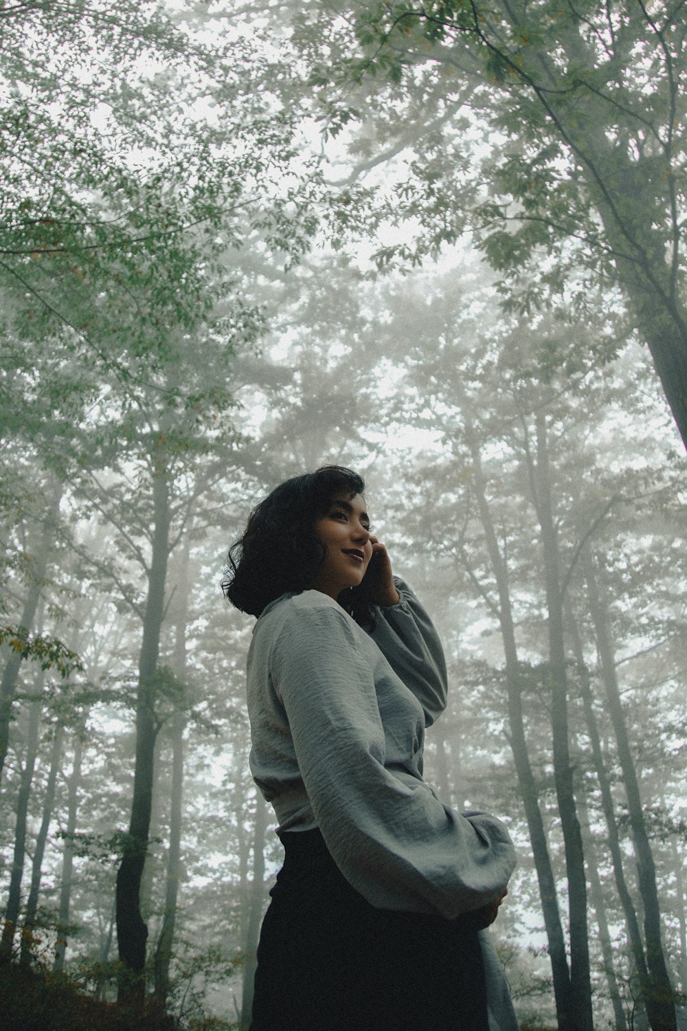 a woman standing in a forest talking on a cell phone