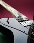 A close-up view of an electric guitar displaying intricate details of its strings, pickups, and controls. The guitar is angled diagonally, with a focus on the fretboard and shiny black body. A deep magenta background contrasts with the instrument's sleek appearance.