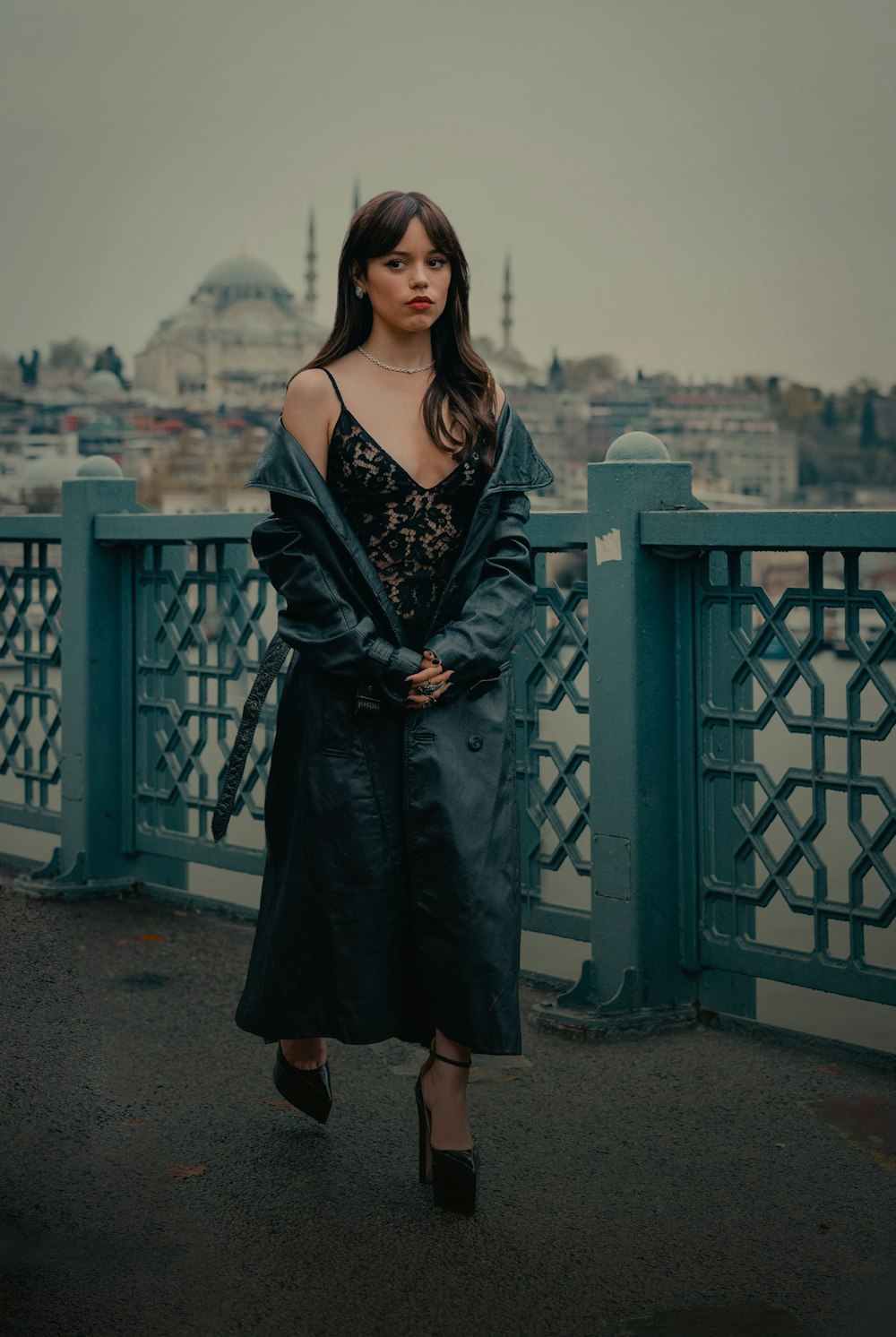 a woman standing on a bridge with a city in the background
