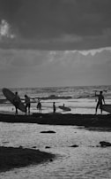 A group of friends carrying surfboards along a sandy beach at dawn.
