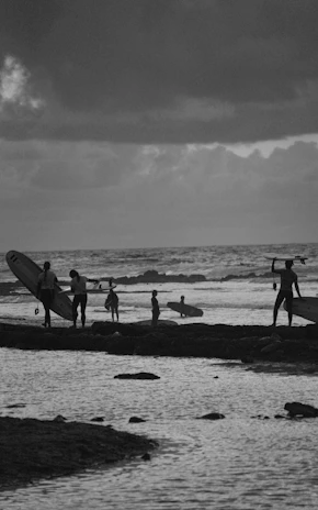 A group of surfers walking along the shore with their boards at sunrise near Jesolo Aruga.