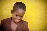 Close-up of a smiling toddler wearing a vibrant yellow jacket and teal shoes from kidsminicloset.