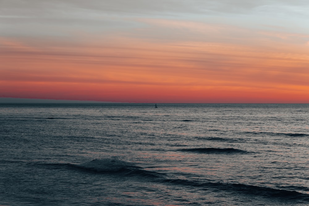 a sunset over the ocean with a sailboat in the distance
