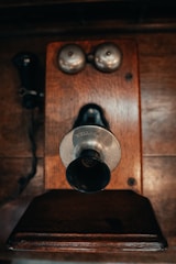 A vintage wall-mounted telephone features a wooden base with metallic bells and a protruding mouthpiece and earpiece. The design is reminiscent of early 20th-century communication devices, reflecting a sense of nostalgia and antique charm.