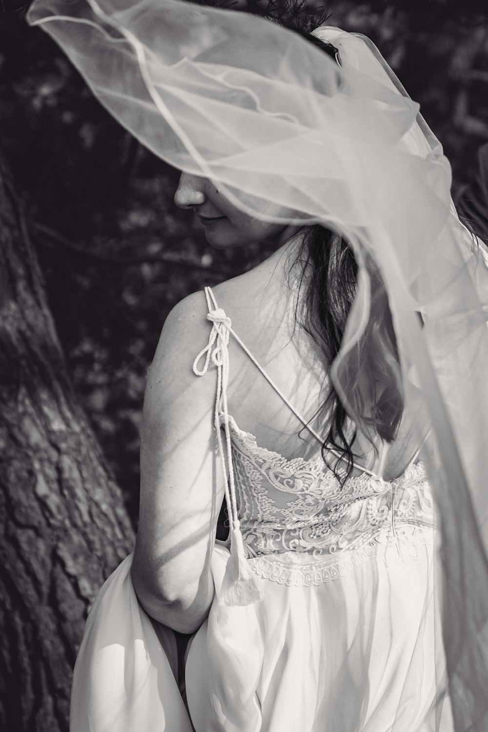 a woman in a white dress and veil standing in front of a tree