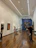 A modern art gallery with wooden flooring and high ceiling, showcasing several paintings on the walls. There are a few people walking around and viewing the artwork. The lighting is bright, emphasizing the artwork.