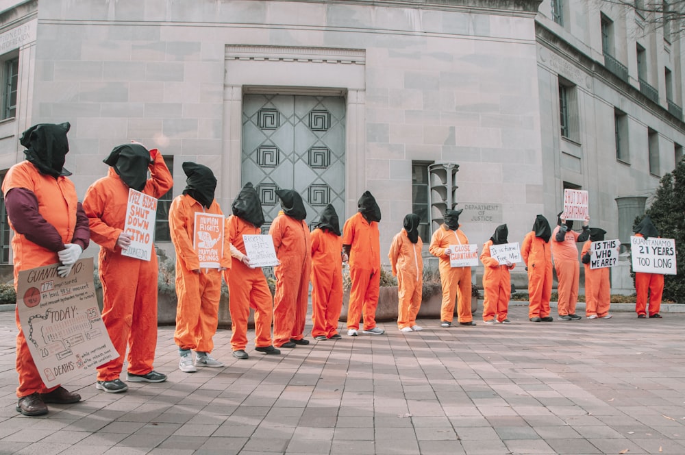 a group of people in orange jumpsuits holding signs