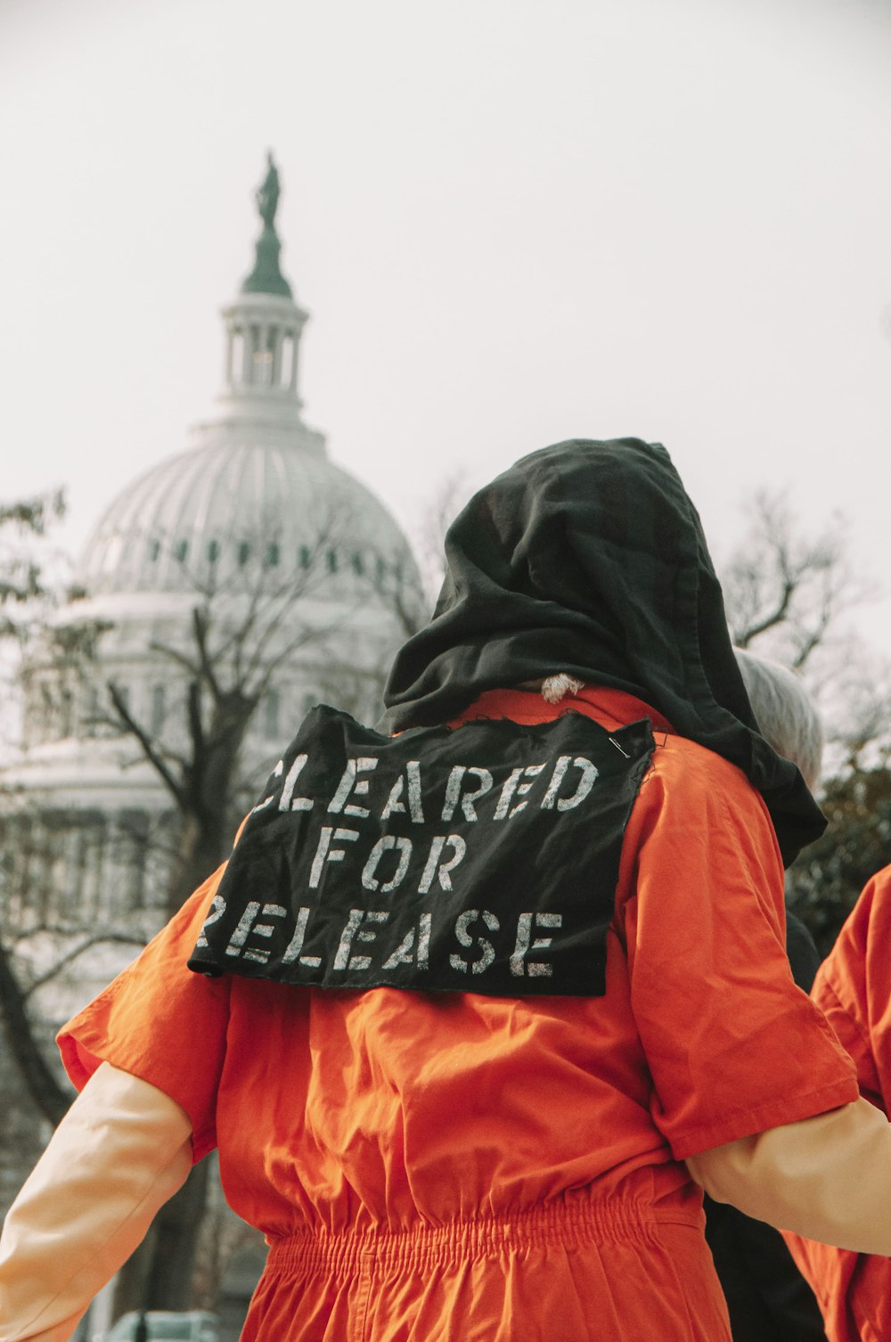 a person in an orange jumpsuit with a black sign on it