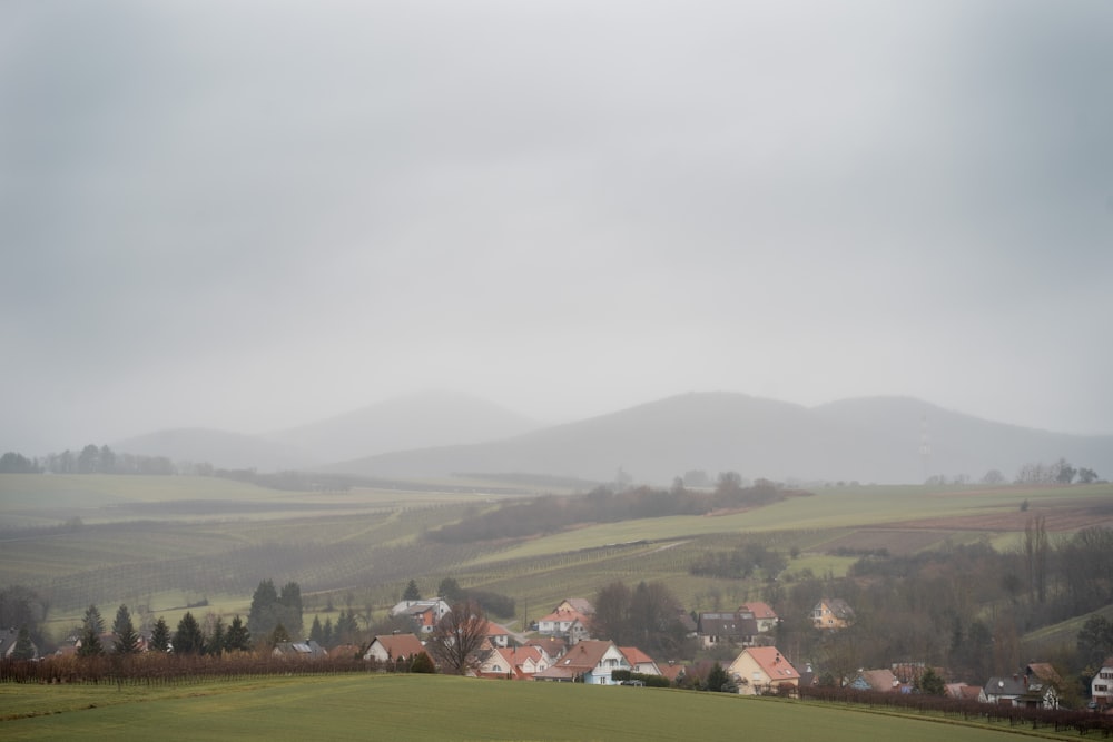 a foggy day in the countryside with houses and hills