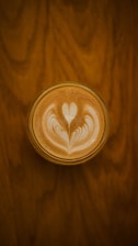 A cup of coffee with intricate latte art featuring a symmetrical heart and floral pattern on the surface.