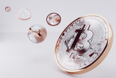 A large, stylized Bitcoin symbol is depicted on a golden coin, surrounded by several floating, reflective spheres with metallic and transparent surfaces.