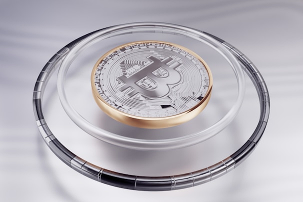 A metallic Bitcoin coin is prominently displayed on a sleek, reflective surface. The coin features detailed circuit-like patterns and the iconic Bitcoin logo. It is encased in a transparent ring, adding to its futuristic and technological appeal.
