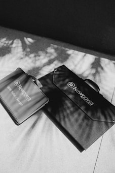 Two portable solar charger bags with handles are placed on a surface with shadows of leaves cast across them. The bags are labeled with 'Newpowa', and they are sleek and modern in design.