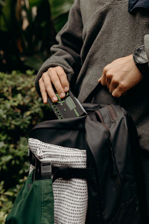 An outdoor enthusiast’s backpack open to reveal a power bank connected to a GPS device on a forest trail.