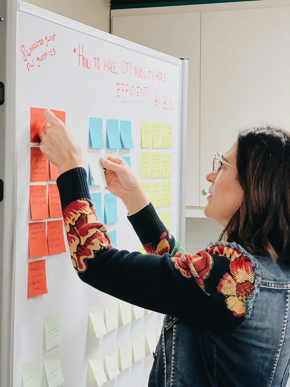 a woman writing on a white board with sticky notes on it