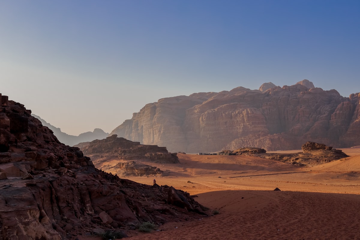 Vast red desert floor with sheer sandstone mesas fading into evening haze in Wadi Rum