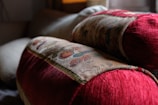 Two intricately patterned cushions with rich red fabric and detailed embroidery rest on a soft surface, creating a cozy and inviting atmosphere in what appears to be a living space with soft lighting.